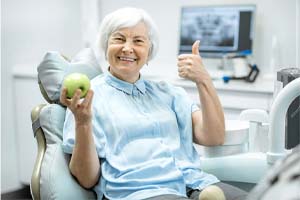 Woman with dental implants in Watertown holding apple and thumbs up
