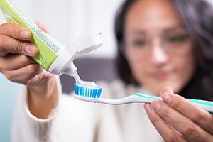 Woman putting toothpaste on brush, preparing to clean her teeth