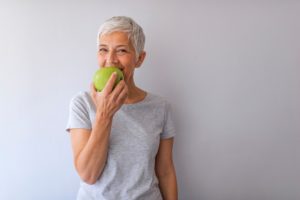 Senior woman enjoying apple with implant dentures in Watertown