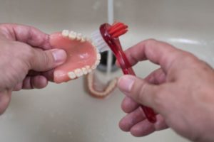 Hands using soft brush to clean dentures over sink