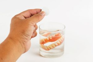 Hand preparing to place cleansing tablet in water with denture